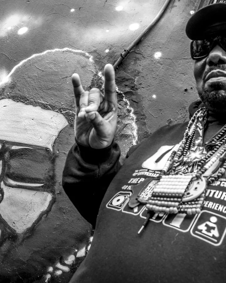 ImageDescription: Afrika Bambaataa next to mural drawing with his face in Bogota during the World Summit of Arts and Culture for Peace in Colombia. Categories: 